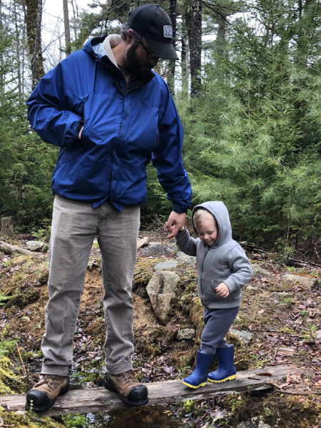 Rory Fraser walks across a small bridge in the forest with his toddler.