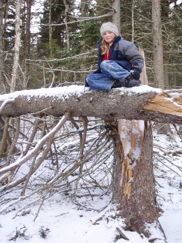 A young Becky sits on a fallen tree in winter.