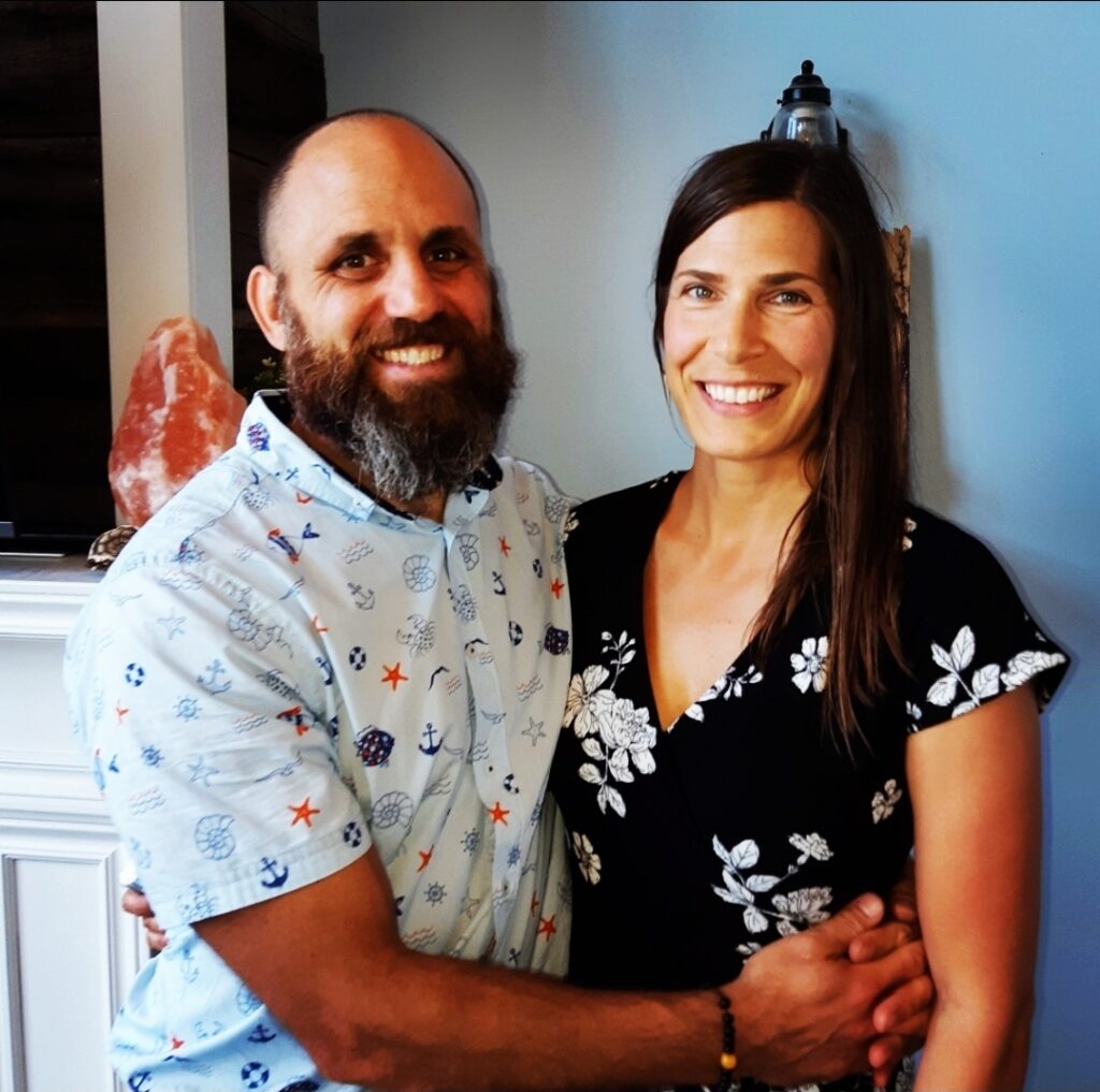 Luciano and Angie embrace and smile and the camera.