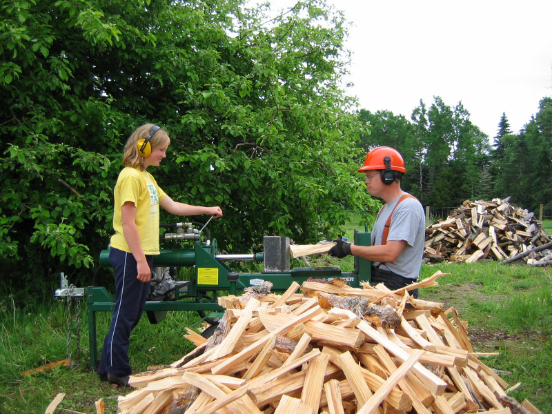 12-year-old Becky splits wood with her father, Kevin, who is wearing a hard hat and sticking his tongue out at her.