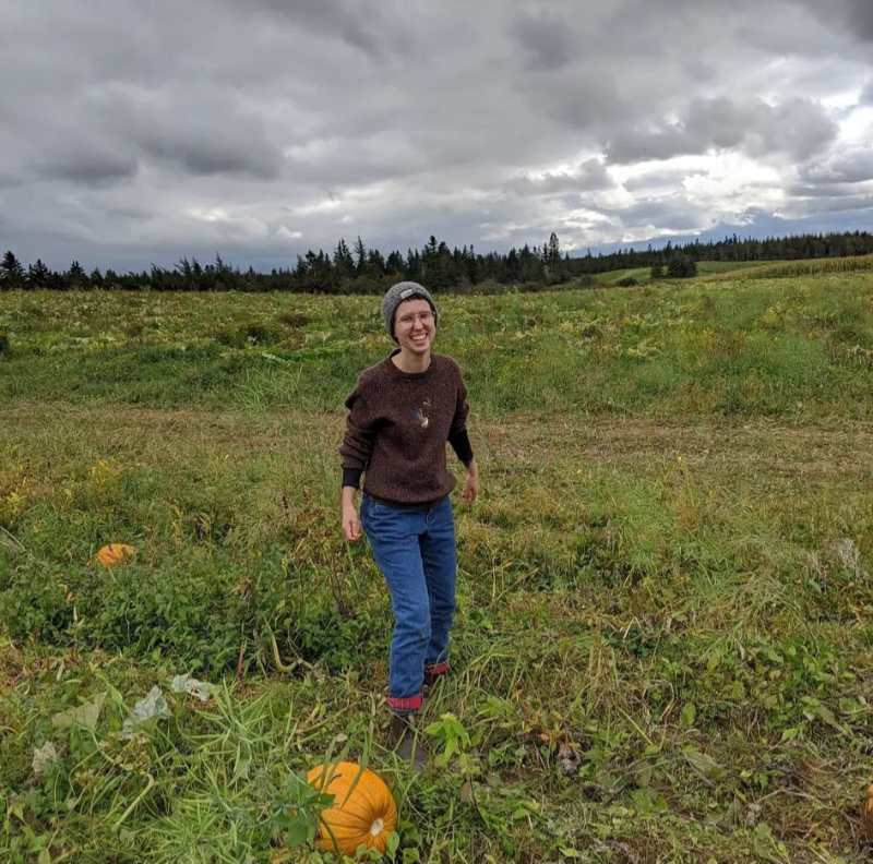 Meg stands in a pumpkin field and smiles.