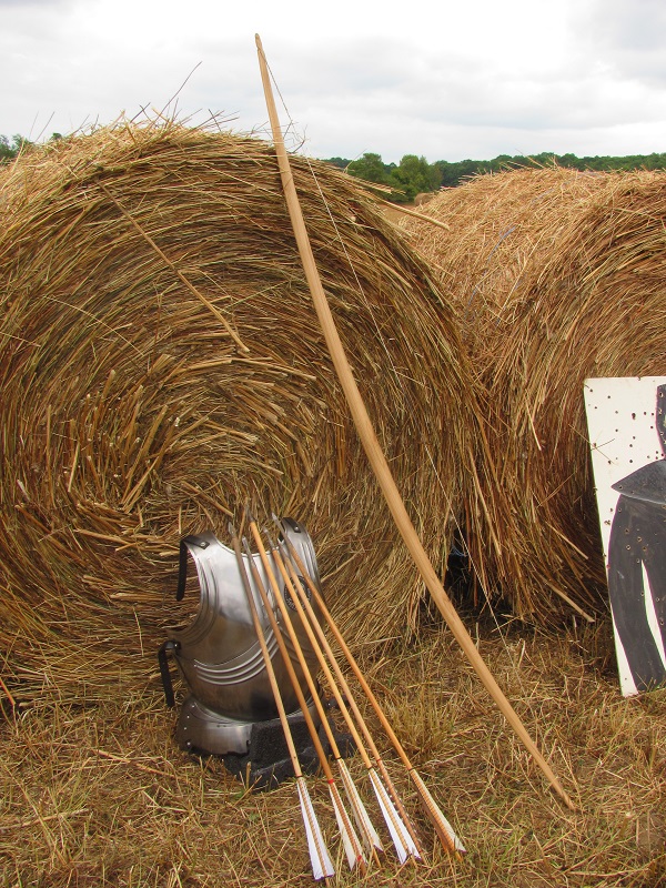 Arrows, a bow, and a breastplate leaning on a hay bale.