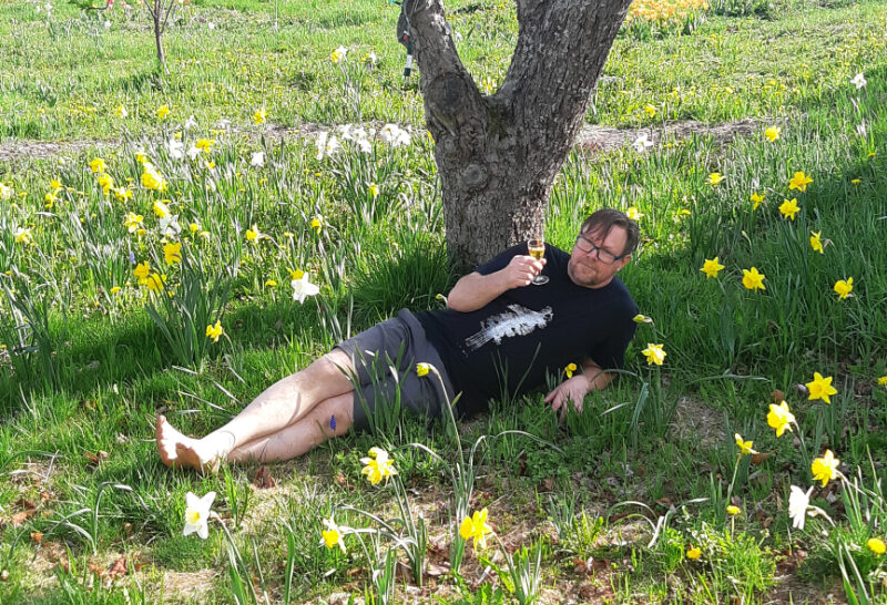 Kevin Anderson enjoys whiskey beneath an apple tree on his lawn, which is flowering with daffodils.