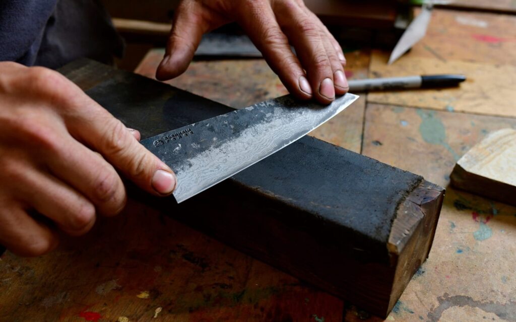 A person sharpens a knife using a whet stone.