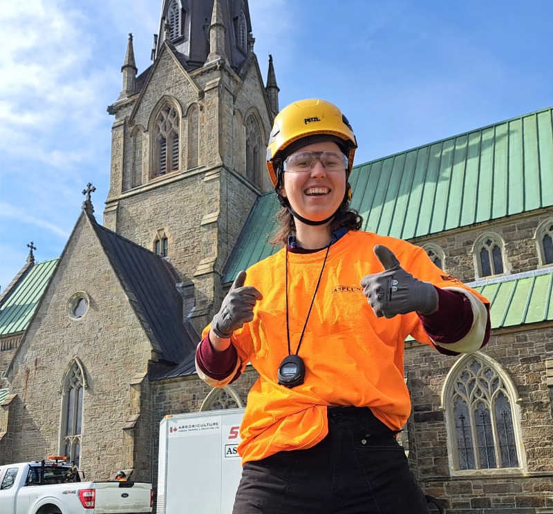 Meg stands in front of a church wearing a helmet and doing double thumbs up