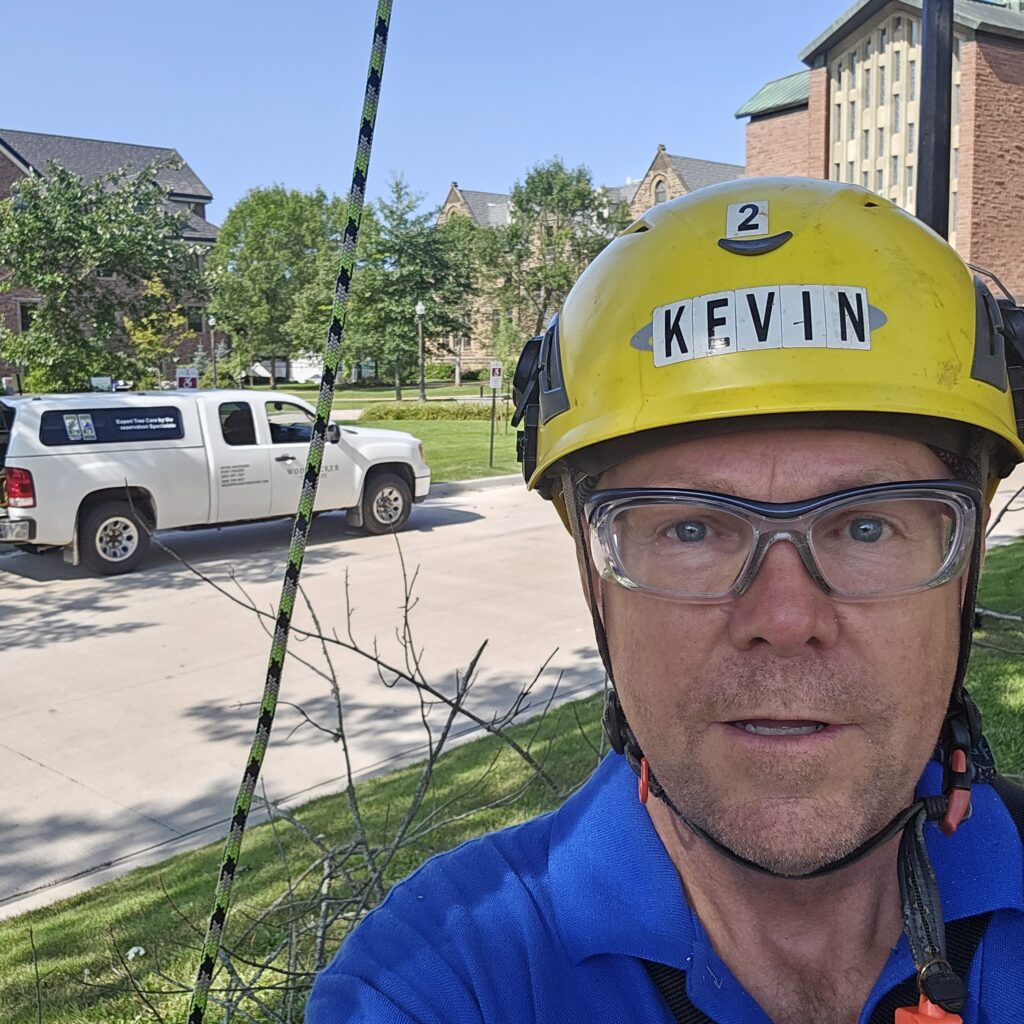 Kevin Anderson wears a Kask helmet with his name on it. He is in front of the Mount Allison chapel. 