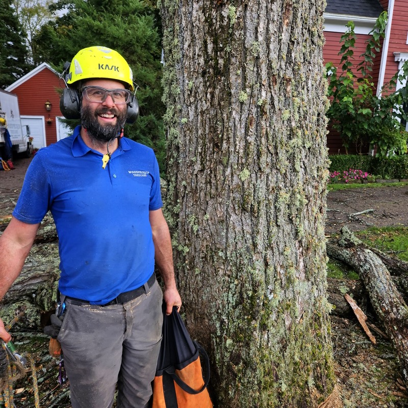 Rory wears a helmet, holds a rope bag, and smiles next to an elm tree.