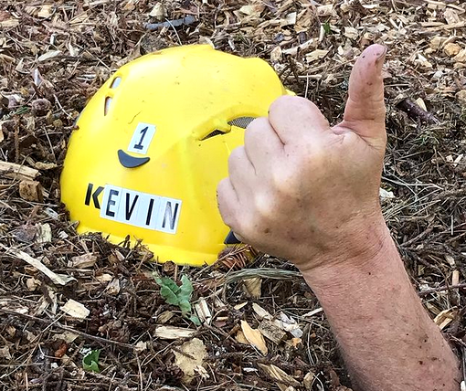 Kevin's helmet rests on wood chips, someone does a thumbs up.